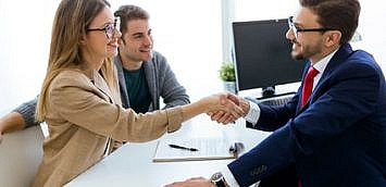 Portrait of young couple in bank office shaking hand to financial adviser.